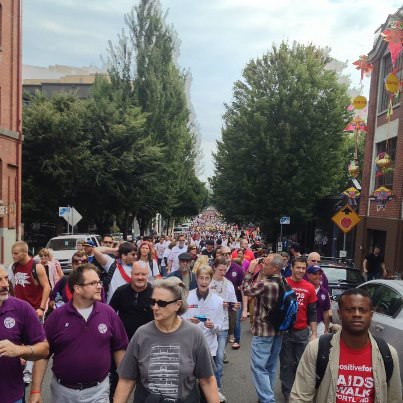 A sea of people walking through The Pearl for AIDS Walk Portland, with Portland Gay Men's Chorus wearing their signature purple shirts.