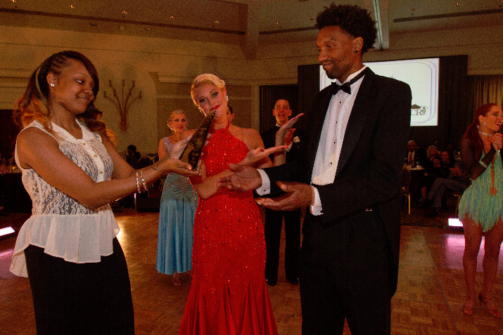 Ifanyi Bell, Digital Producer for OPB, and Fred Astaire Dance Studio’s Jessi Aillon (in red) accept the winning trophy from gala volunteer Alex Morris.