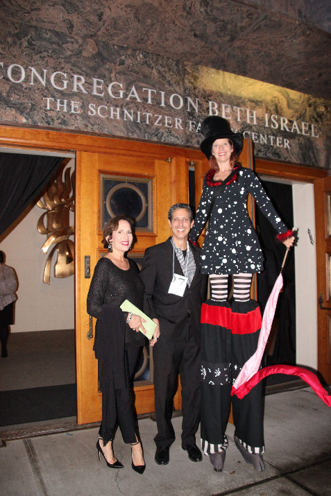 Cantor Ida Rae and Rabbi Michael Cahana join a stilt-walking entertainer to welcome arriving guests at the doorway to Schnitzer Family Center.