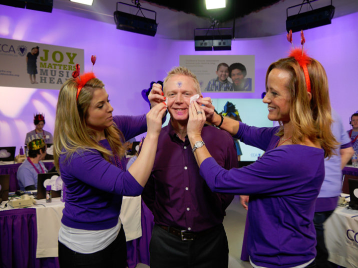 Betsy Reed, Business Developer, and Allison Clarke, President Allison Clarke Consulting and CCA Ambassador Board Co-Chair, add two purple heart tattoos to Fox 12 Oregon’s Any Carson’s cheeks to fulfill a viewer request in exchange for a $2,000 dollar donation.