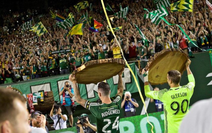 Fans love getting out of the stands and volunteering side-by-side with their favorite players. (This photo is from June 1st as Portland Timbers defender Liam Ridgewell (24) and goalkeeper Jake Gleeson (90) hold up log slabs after the 1-0 win at Providence Park. Photo: Craig Mitchelldyer) 