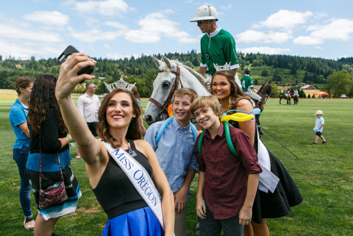 Miss Oregon 2016, Alexis Mather and Miss Oregon Outstanding Teen 2016, Abigail Hoppe, pose for a selfie with two young guests and polo players on the field.
