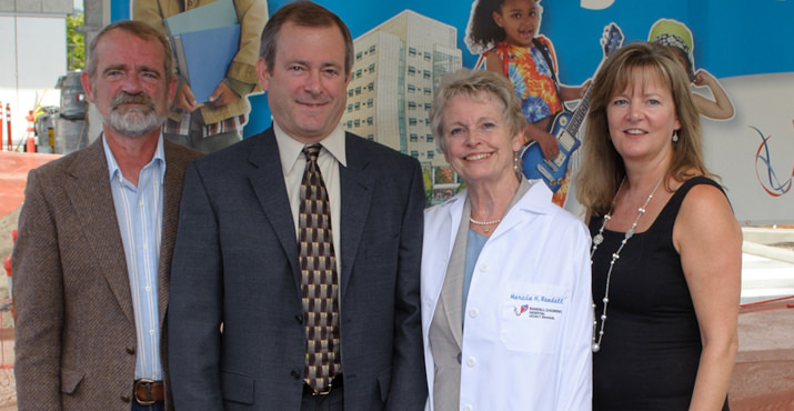 Dick Norgart, Mary Norgart, Marcia H. Randall, and Kristin Randall with a red wagon featuring the new name: Randall Children’s Hospital at Legacy Emanuel.