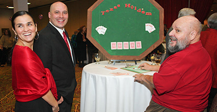 Solen(left) and Jeremy Wilebski consider buying into the Texas Hold 'Em game hosted by Jim Klum (not shown) detailed by past auction chair Tom Weldon (Rt). They decide their poker face is not sufficient, but enjoy an evening of revelry and fine dining benefitting SnowCap Community Charities.