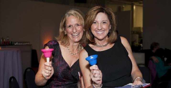 Event committee members Cynthia Hofmann and Shelly Levy ring bells during the Mitzvah Moment paddle raise to signal another donation made.